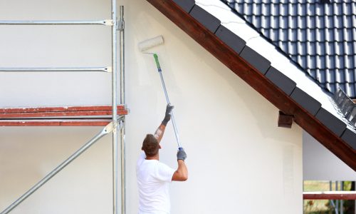 Malowanie wałkiem elewacji budynku na rusztowaniu.